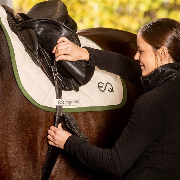 Eine Frau befestigt eine Schabracke an einem Pferd